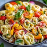 A vibrant bowl of cheese tortellini tossed with zucchini, cherry tomatoes, bell peppers, and fresh basil, drizzled with olive oil.
