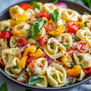 A vibrant bowl of cheese tortellini tossed with zucchini, cherry tomatoes, bell peppers, and fresh basil, drizzled with olive oil.
