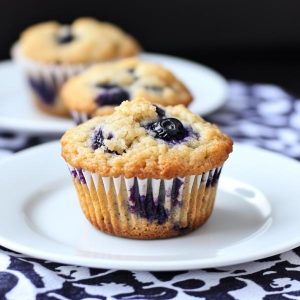A batch of golden blueberry muffins with juicy berries peeking through, served on a rustic tray with a side of fresh blueberries.