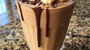 A tall glass of chocolate peanut butter banana shake topped with whipped cream, chocolate drizzle, and sliced bananas.