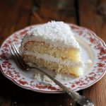 Moist coconut cake topped with fluffy coconut frosting and sprinkled with shredded coconut.