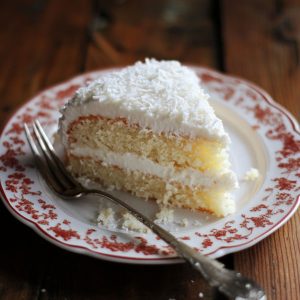 Moist coconut cake topped with fluffy coconut frosting and sprinkled with shredded coconut.