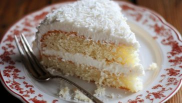 Moist coconut cake topped with fluffy coconut frosting and sprinkled with shredded coconut.