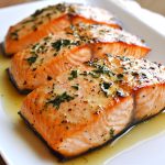 Salmon fillet roasted in butter, golden and flaky, garnished with lemon slices and fresh herbs.