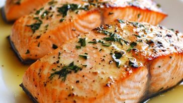 Salmon fillet roasted in butter, golden and flaky, garnished with lemon slices and fresh herbs.