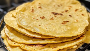 Stack of warm homemade corn tortillas on a rustic plate, soft and golden with a slightly charred surface.
