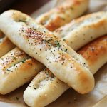 Golden, fluffy breadsticks brushed with garlic butter, stacked on a serving tray with a side of marinara sauce.