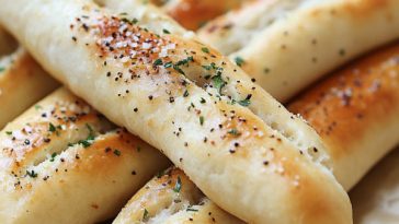 Golden, fluffy breadsticks brushed with garlic butter, stacked on a serving tray with a side of marinara sauce.
