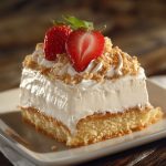 Moist tres leches cake soaked in three milks, topped with whipped cream and fresh strawberries on a white plate.
