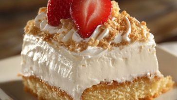 Moist tres leches cake soaked in three milks, topped with whipped cream and fresh strawberries on a white plate.