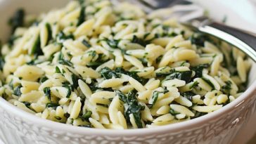 A bowl of creamy orzo pasta mixed with fresh spinach and topped with grated parmesan cheese, garnished with cracked black pepper.