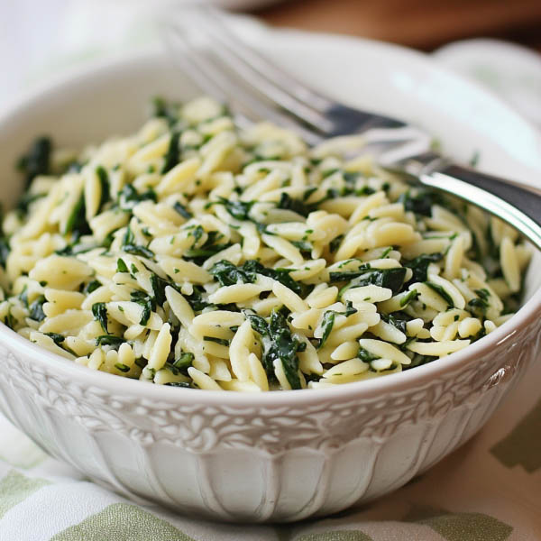 A bowl of creamy orzo pasta mixed with fresh spinach and topped with grated parmesan cheese, garnished with cracked black pepper.