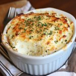 Golden baked parmesan mashed potatoes topped with melted cheese and crispy edges, served in a casserole dish.