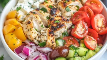 Greek chicken bowls with marinated grilled chicken, fresh cucumber, tomato, olives, feta, and tzatziki sauce served over rice.