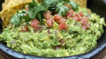 Fresh guacamole made with ripe avocados, lime juice, cilantro, onions, and tomatoes served in a rustic bowl with tortilla chips.