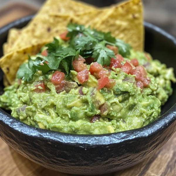 Fresh guacamole made with ripe avocados, lime juice, cilantro, onions, and tomatoes served in a rustic bowl with tortilla chips.