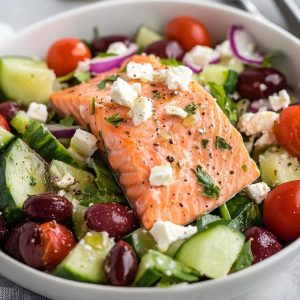 A vibrant Greek salmon salad with baked salmon fillet, romaine lettuce, tomatoes, cucumbers, olives, feta, and lemon-mint vinaigrette.
