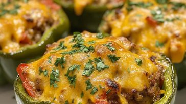 Colorful bell peppers stuffed with seasoned rice, ground meat, vegetables, and melted cheese, baked golden in a casserole dish.
