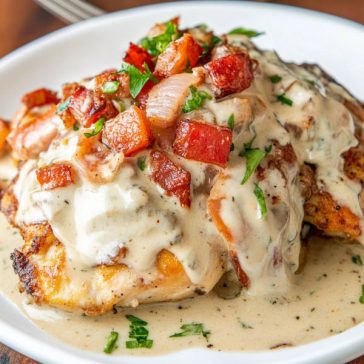 Juicy chicken breasts smothered in melted cheese, crispy bacon, fresh tomatoes, and lettuce, served on a rustic plate.