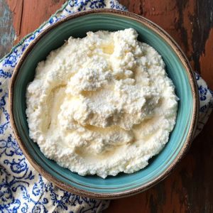 A bowl of freshly made ricotta cheese with a soft, creamy texture, garnished with basil and served with crusty bread.