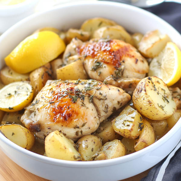 Greek slow cooker lemon chicken with golden potatoes, garnished with herbs and lemon slices in a rustic serving dish.