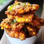 Golden crispy corn fritters stacked on a plate with dipping sauce