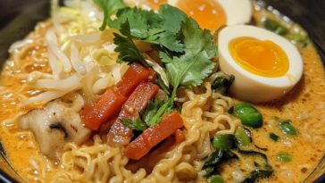 Bowl of Thai coconut curry ramen with noodles, vegetables, and fresh herbs