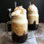 Tall glass of vanilla bean root beer float topped with whipped cream and a cherry.