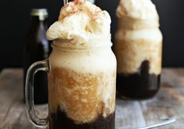 Tall glass of vanilla bean root beer float topped with whipped cream and a cherry.