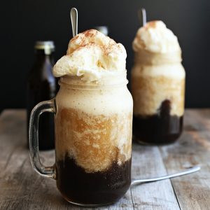 Tall glass of vanilla bean root beer float topped with whipped cream and a cherry.