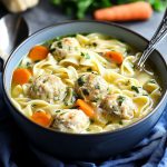 Bowl of chicken meatball noodle soup with fresh herbs and vegetables.