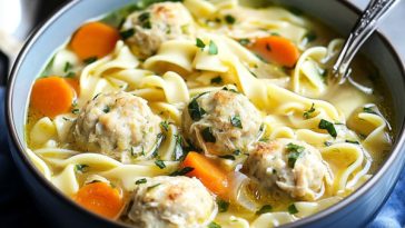 Bowl of chicken meatball noodle soup with fresh herbs and vegetables.