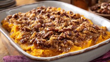 Sweet potato casserole with golden pecan topping in a baking dish, garnished with fresh herbs.