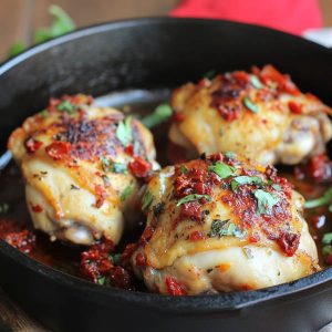 Skillet of chicken thighs in creamy sun-dried tomato sauce garnished with fresh herbs