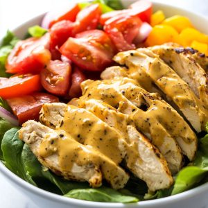 Bowl of honey mustard chicken salad with fresh greens, grilled chicken, and drizzled dressing.