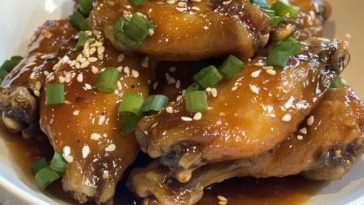 Sticky glazed chicken wings served on a platter with sesame seeds and green onions.