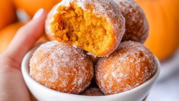Golden pumpkin donut holes rolled in cinnamon sugar on a rustic plate.