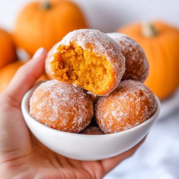 Golden pumpkin donut holes rolled in cinnamon sugar on a rustic plate.