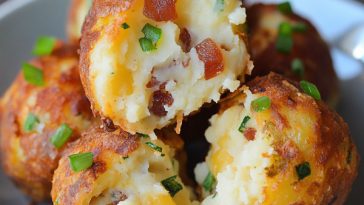 Golden fried mashed potato balls stuffed with melted cheese, bacon, and chives, served on a platter.