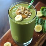 Green smoothie with peanut butter and banana served in a tall glass with a straw.
