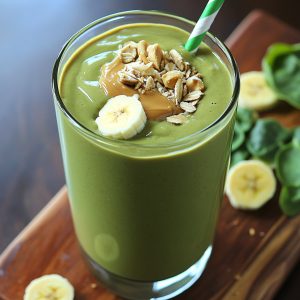 Green smoothie with peanut butter and banana served in a tall glass with a straw.