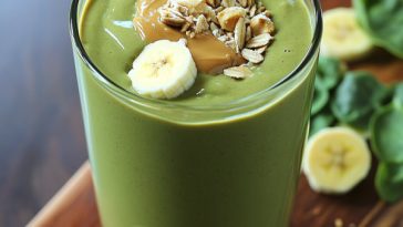 Green smoothie with peanut butter and banana served in a tall glass with a straw.
