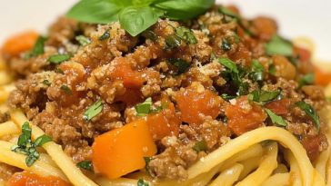 Bowl of pasta topped with turkey bolognese sauce and fresh basil.