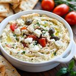 Bowl of creamy Greek feta dip garnished with olive oil and fresh herbs.