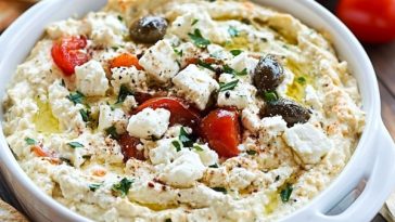 Bowl of creamy Greek feta dip garnished with olive oil and fresh herbs.