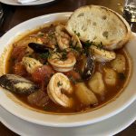 Cioppino seafood stew served in a rustic bowl with clams, mussels, shrimp, scallops, and fish simmered in a tomato-based broth, garnished with fresh parsley and crusty bread.