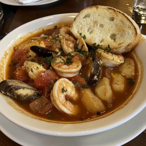 Cioppino seafood stew served in a rustic bowl with clams, mussels, shrimp, scallops, and fish simmered in a tomato-based broth, garnished with fresh parsley and crusty bread.