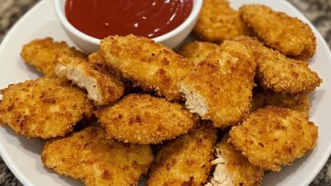 Baked chicken nuggets served on a plate, golden brown and crispy, paired with dipping sauces and garnished with parsley.