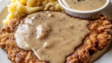 Chicken fried steak topped with creamy country gravy, served with mashed potatoes and garnished with fresh parsley on a rustic plate.