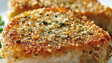 Golden brown Parmesan-crusted pork chops served on a plate with fresh herbs, crispy coating, and juicy interior, paired with roasted vegetables.